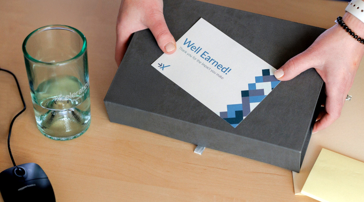 Hands opening a Well Earned! reward gift box on a desk