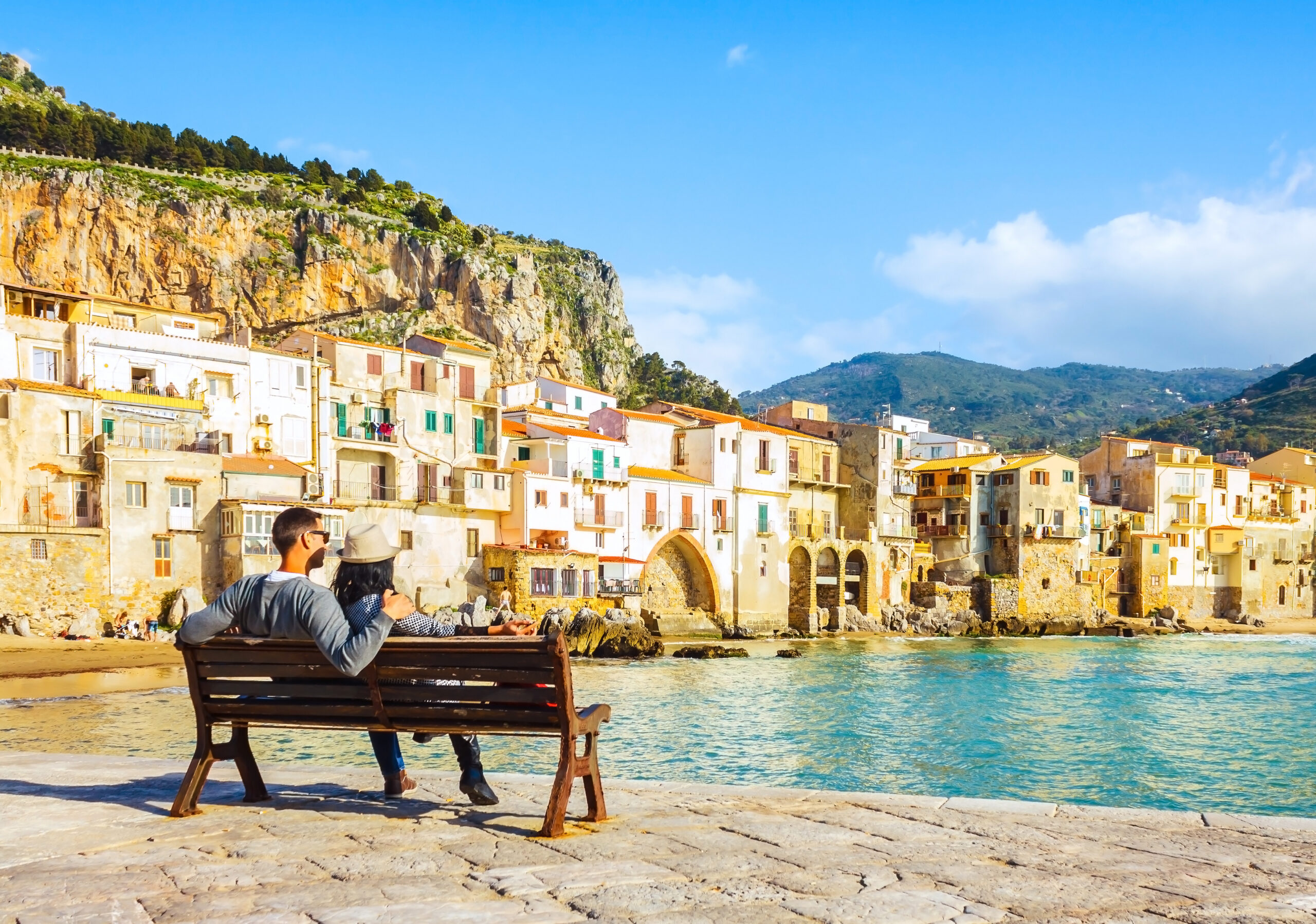 A couple sitting on a bench looking out over a seaside town.